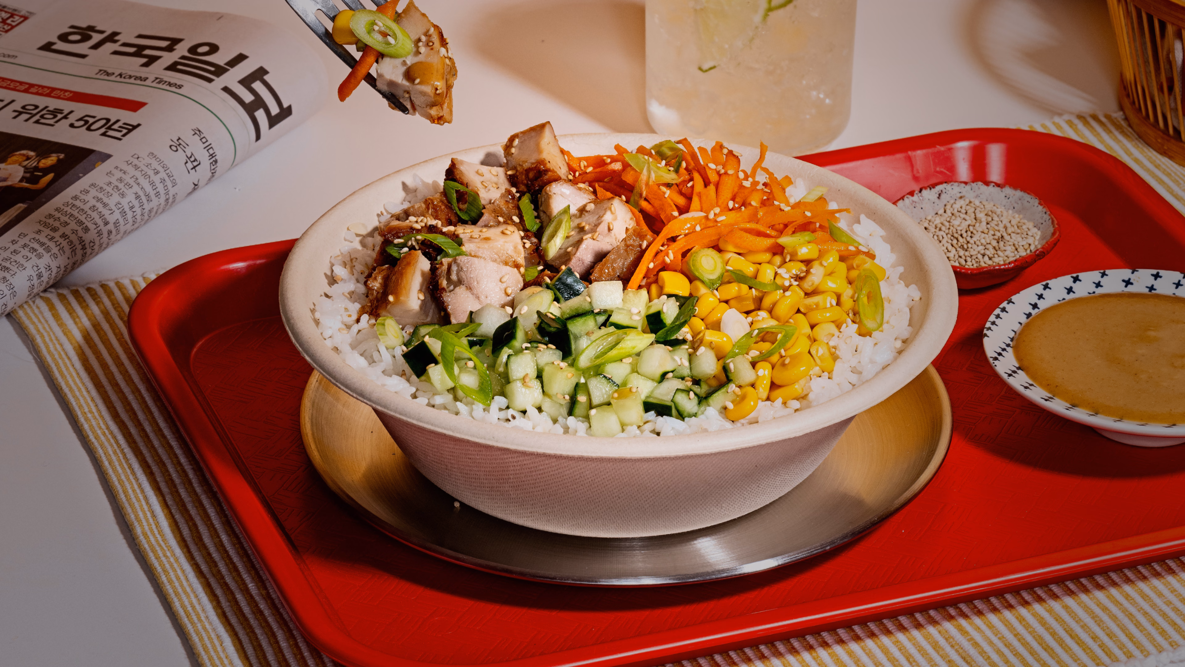 Rice bowl with sliced meat, cucumbers, corn and carrots on a red tray